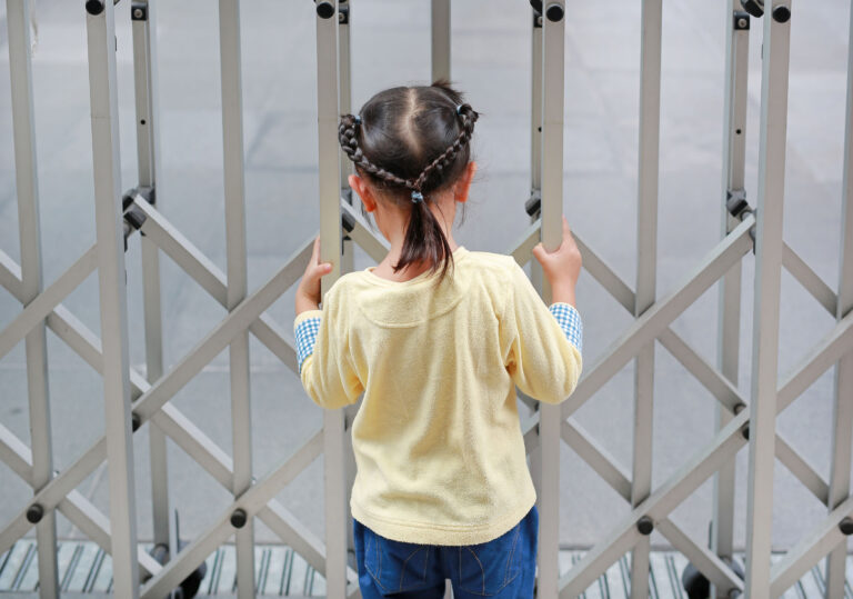 Back view of child girl holding steel fence.
