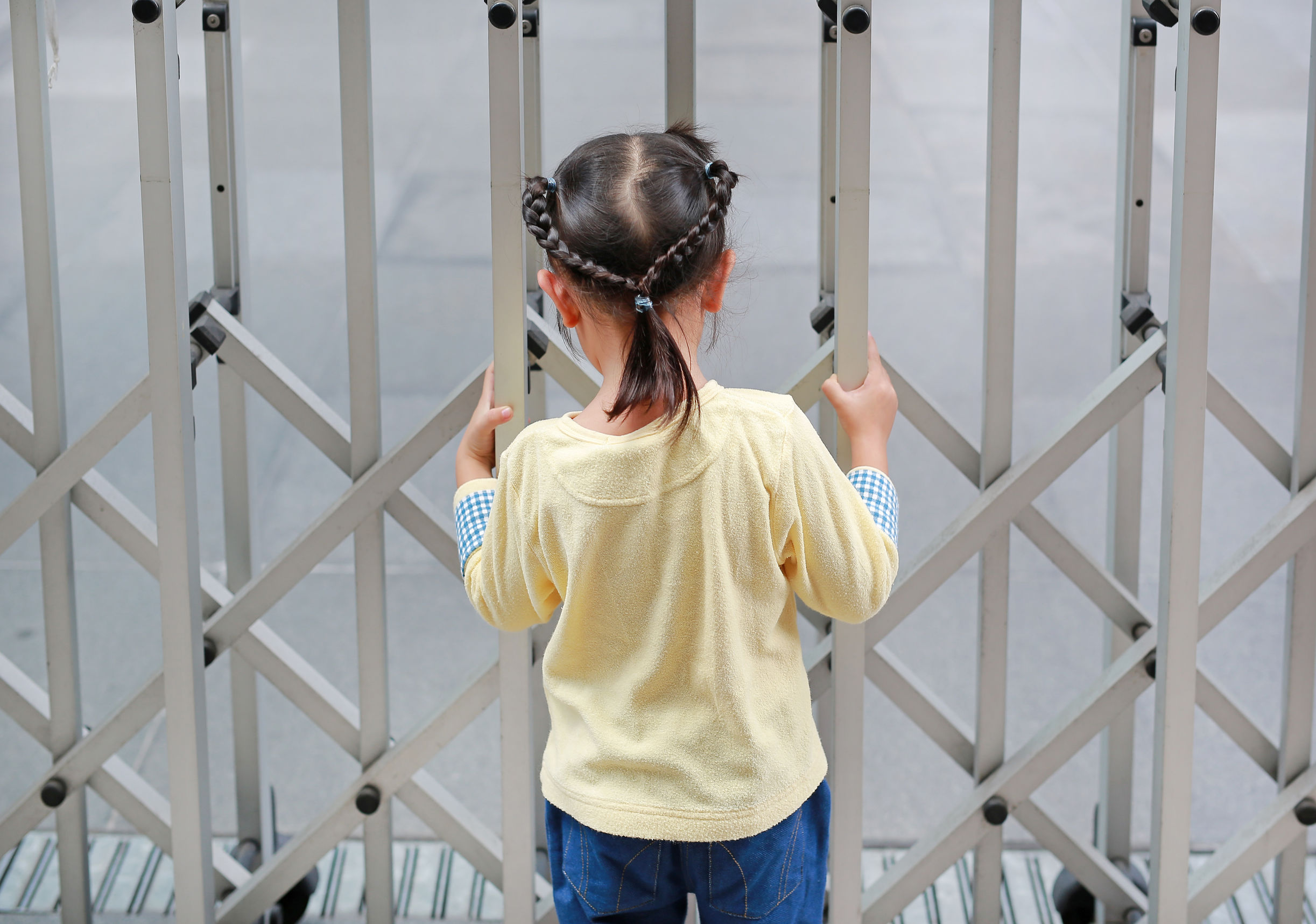 Back view of child girl holding steel fence.