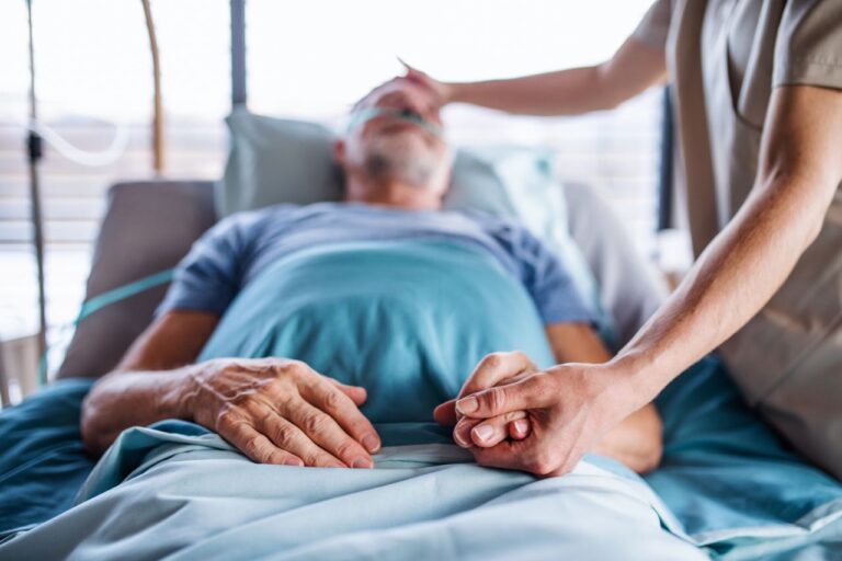 Unrecognizable female doctor examining senior man in bed in hospital.