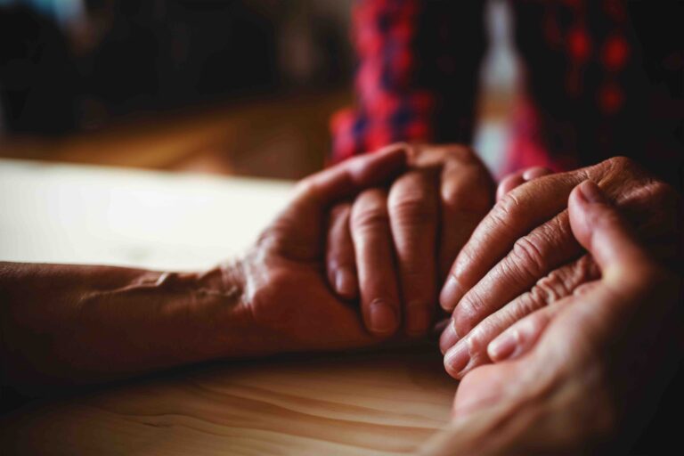 Close-up of senior couple holding hands at home