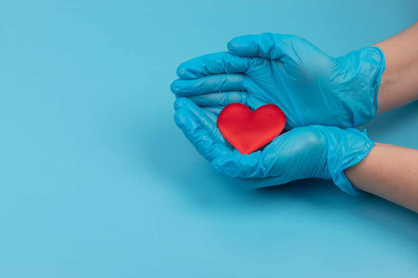 Red heart in hands in blue medical gloves on blue background. Background for the day of the medic. World Heart Day. Heart diseases.
