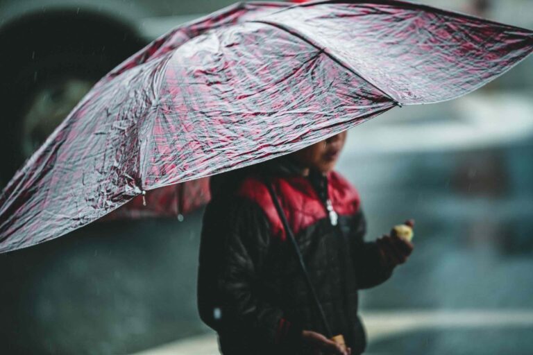 Young local Sapa boy walks through the small mountain village in Vietnam, Asia eating an apple and holding an umbrella up to protect him from the rain.