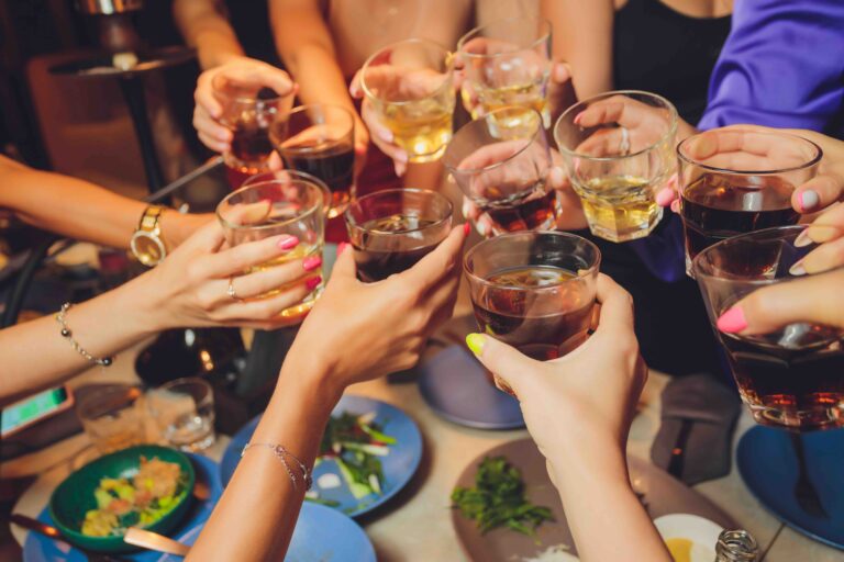Close up shot of group of people clinking glasses with wine or champagne in front of bokeh background. older people hands.