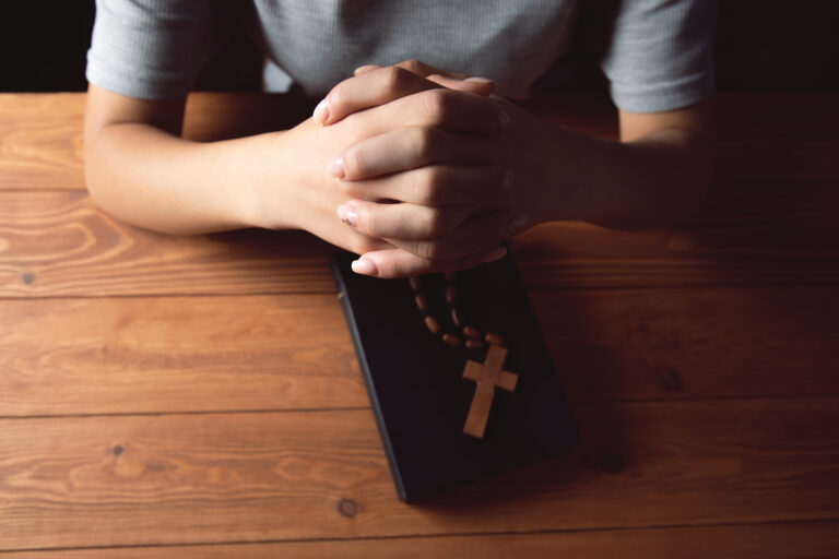 woman praying on book holding cross