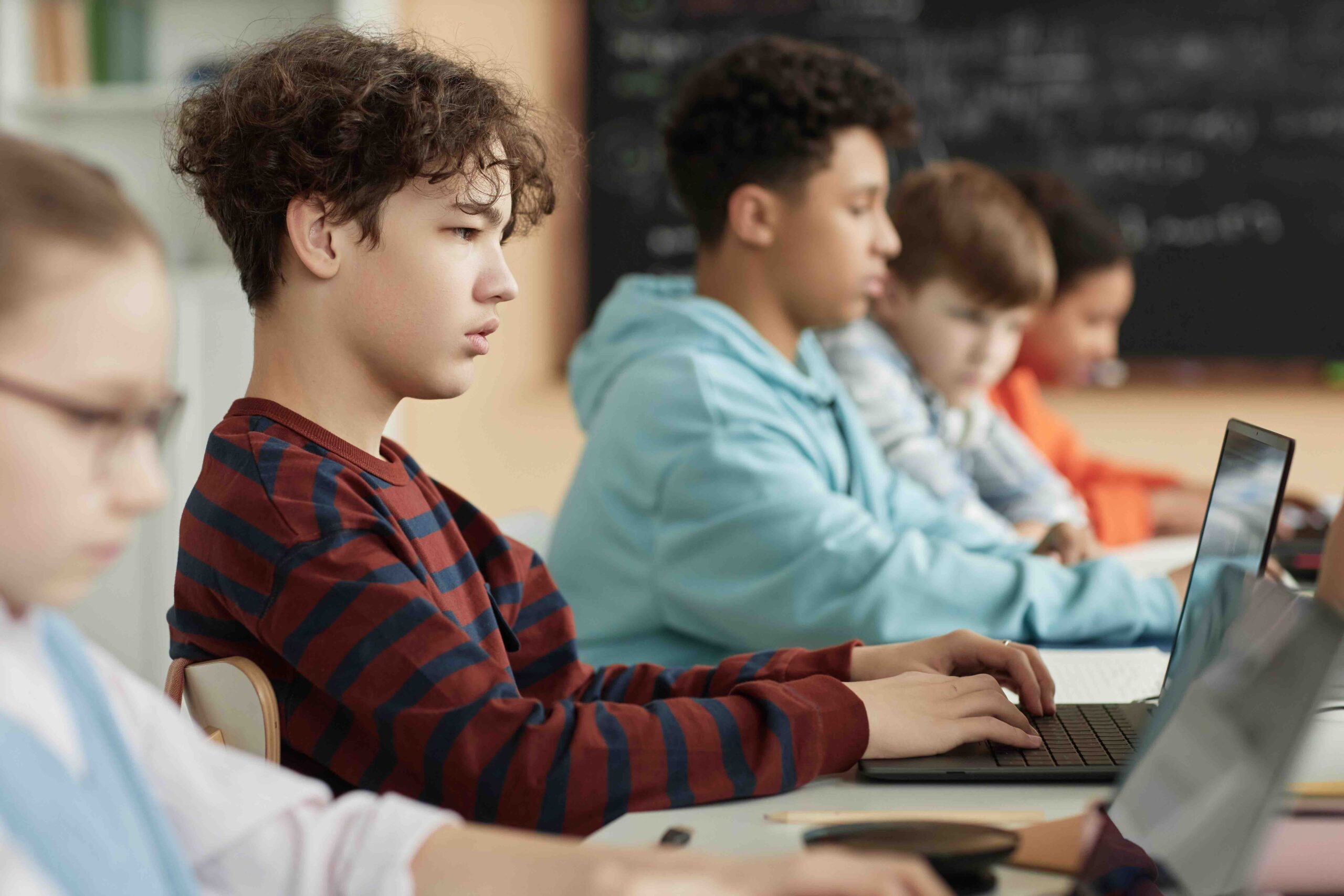 Boy using computer in row in school classroom and taking online exam