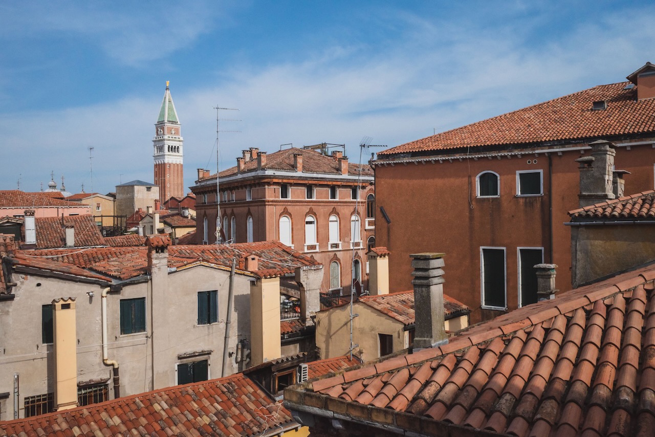 San Marco bell tower over traditional Venetian houses under blue sky in Venice, Italy