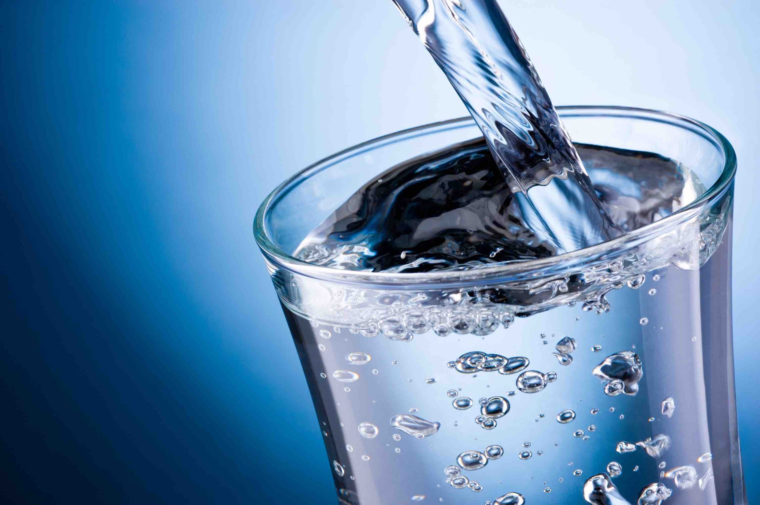 Water pouring into glass on blue background