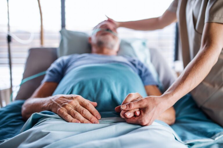 Unrecognizable female doctor examining senior man in bed in hospital.